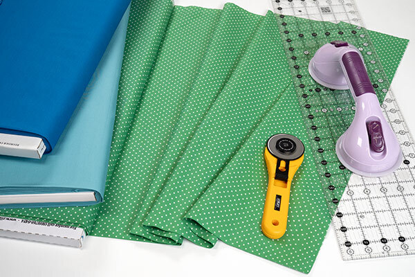 A collection of green polka-dotted fabric pieces, a rotary cutter, and a quilting ruler on a table.