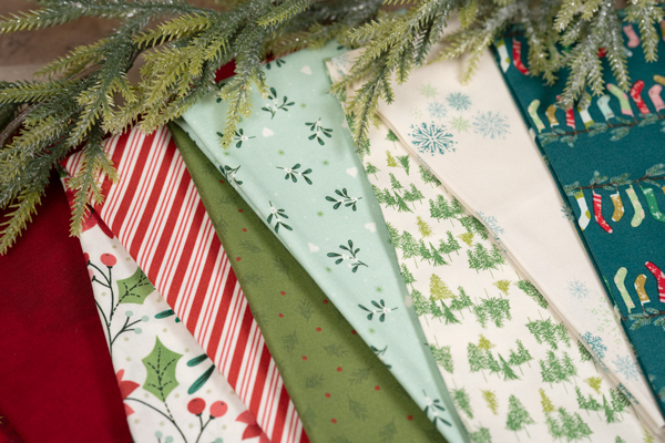 A array of patterned fabrics in red, green, and white, with holiday-themed designs and greenery.