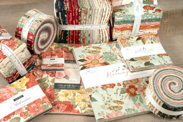 Bundles of colorful fabric rolls and squares with floral patterns arranged on a wooden surface.