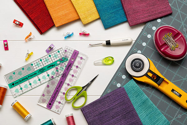A variety of colorful fabric swatches, quilting tools, scissors, and threads arranged on a table.
