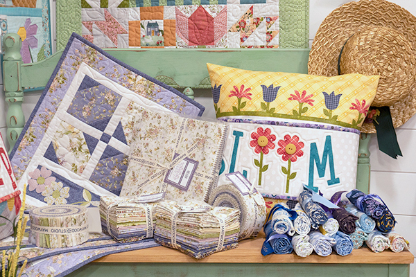 Quilts, fabric bundles, and quilt kits displayed on a bench in a bright setting