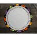 A round decorative mat with a white center and a colorful scalloped border, featuring Halloween-themed designs such as pumpkins and ghosts. The text around the edge reads, “Tick or treat, smell my feet. Give me something good to eat!”