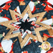 A circular quilted design featuring a star pattern, constructed with various fabrics in red, beige, and dark blue, showcasing festive holiday-themed illustrations and plaid textures at the points of the star.