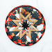 A round fabric quilted coaster featuring a star pattern. The design includes various colors, primarily black, red, white, and brown, with festive winter gnomes.