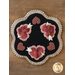 A decorative round rug featuring four red flowers with white accents and pink hearts, set against a black background. The rug has a scalloped beige border.