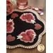 A decorative table mat featuring pink and red hearts, some with arrows, set against a black background. The mat has a scalloped edge and is embellished with small pearls. In the background, there is a blurred pink rose and shiny buttons.