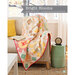 A colorful, patchwork quilt drapes over a beige couch with a book and clock on a nearby table.