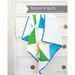 A colorful quilt displayed against a white wooden dresser, featuring triangles in blue, green, and yellow.