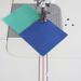 A sewing machine needle is positioned above two pieces of fabric, one teal and one blue, that are overlapping at a corner.