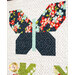 A quilt design featuring a butterfly made of fabric patches. The butterfly's wings are patterned with colorful flowers on a dark background, and the body is made of a light blue fabric. The quilt has a white background with subtle polka dots and green leaf designs at the bottom.