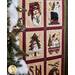 A festive quilt featuring nine panels with various snowman designs, including snowmen in hats, with trees, and in a wagon. Surrounding the quilt are Christmas decorations and a tree.