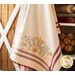 A decorative kitchen towel hangs from a shelf, featuring the text FARM GIRL surrounded by illustrations of vegetables and flowers. The towel has red stripes and pom-pom trim at the bottom.