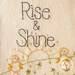 Embroidered design featuring the words Rise & Shine above a stylized sun and two cheerful chicks, with decorative green elements.