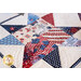 A close-up of a quilt featuring a star pattern with red, white, and blue fabrics, including images of fireworks, stars, and stripes, symbolizing patriotic themes.