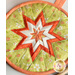 A circular pot holder featuring a star-shaped design with layers of floral green fabric and contrasting orange accents. The star is centered within the pot holder, surrounded by a peach-colored border.