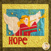 A colorful quilted panel featuring an angel playing a trumpet. The background includes a bright blue sky with stars, and the word HOPE is prominently displayed in red letters at the bottom. The angel has golden hair and white wings, and is dressed in a striped red and green outfit.