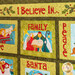 A quilt featuring decorative squares with colorful fabric illustrations and text. The top includes the phrase I Believe In... followed by the words FAMILY, PEACE, and SANTA prominently displayed in various squares. Each square contains imagery associated with the themes.