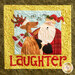 A festive quilted wall hanging features a smiling reindeer and Santa Claus, with text below that reads LAUGHTER. The background is a cheerful yellow with decorative stitching.