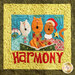 A colorful quilted design featuring three cartoonish cats singing together with a songbook. The background is bright with a blue section behind the animals and a green border. The word HARMONY is prominently displayed in bold red letters at the bottom.