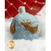 A decorative blue felt Christmas ornament featuring two brown reindeer with embroidered details. The ornament is embellished with white stitching and small red beads, resting on a bed of soft, white fluff, with a red and gold background.