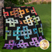 A colorful quilt featuring intricate patterns of interconnected shapes on a black background.