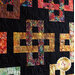 Colorful quilt featuring intricate patterns in squares and crosses against a black background.