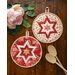 two hot pads on a wood table with wooden spoons and pink flowers