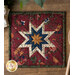 Red hot pad with central folded star designs and navy fabric resting on a wood table.