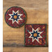 Two red hot pads with central folded star designs and red fabric resting on a wood table.