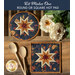 Two dark blue hot pads with central folded star designs and navy fabric resting on a wood table next to spoons and flowers.