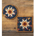 Two dark blue hot pads with central folded star designs and navy fabric resting on a wood table.