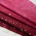 Three layers of fabric in shades of pink and burgundy, adorned with gold specks and dots, arranged neatly.