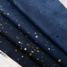 A close-up of navy fabric featuring scattered gold and black paint splatters. The fabric is folded in layers, showing a textured pattern.