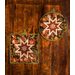 Two autumn themed floral hot pads with a central folded star design on wooden table.