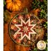 Round autumn themed floral hot pad with a central folded star design on wooden table next to small pumpkins.