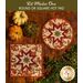 Two autumn themed floral hot pads with a central folded star design on wooden table next to small pumpkins.