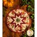 Round autumn themed floral hot pad with a central folded star design on wooden table next to small pumpkins.