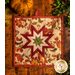 Square autumn themed floral hot pad with a central folded star design on wooden table next to small pumpkins.