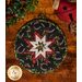 Round hot pad made of black fabric with tossed horseshoes and holly featuring a central folded star.