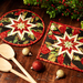 Two black hot pads with central folded star, featuring cardinals and holly.