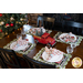 Christmas themed scalloped placemats featuring red trucks, wagons, and pine trees as part of a table setting with plates and cloth napkins.