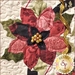 A close-up of a decorative quilt featuring a large, multi-colored flower with shades of red, pink, and black, surrounded by green leaves, and embellished with golden beads at the center. There is a gold ribbon nearby, and the bottom right corner displays a logo for Shabby Fabrics.