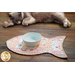 Fish shaped cat pet placemat made of strips of pink and cream cat themed fabrics holding a white bowl near a resting cat.