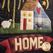 A patchwork design featuring a house with a heart-shaped window, a sheep, a tree, and the word HOME prominently displayed in bold letters at the bottom.