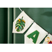 A banner featuring two decorative felt pieces; one has a colorful tropical leaf design, and the other displays a green letter A on a white background. The banner is hanging on a green wall.