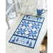 Blue and white winter themed table runner atop a white counter with a wintry scene outside an adjacent window and snowflake decorations with a mug of hot cocoa.