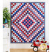 Red, white, and blue quilt of squares in diamond pattern with patriotic themed fabrics hanging from a white panel wall.