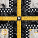 Wall hanging with four blocks made of strips of bee themed and floral fabrics in white, black, and yellow.