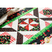 A colorful patchwork quilt featuring red, black, and white fabrics with patterns of strawberries, checkered designs, and geometric shapes arranged on a table.