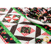 A decorated table with a quilted table runner featuring a geometric pattern in red, black, and white, adorned with strawberry motifs. There is a stack of fabric napkins with a similar design next to a plate.